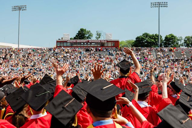 Photo: Commencement 2022 crowd facing the audience and waving at them. They were their cap and gown--black cap, red gown--on a bright, sunny day.