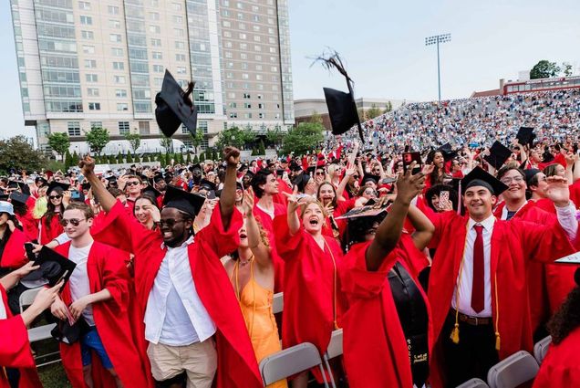 This is a photo from a past Boston University commencement ceremony. Students are seen celebrating and throwing their caps up in the air.