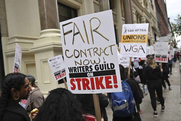 Photo: A group of strikers hold up signs protesting the unfair decisions and contracts made for writers in the writer guild. The prompt sign in the middle of the photo reads: "FAIR CONTRACT NOW! WRITERS GUILD ON STRIKE"
