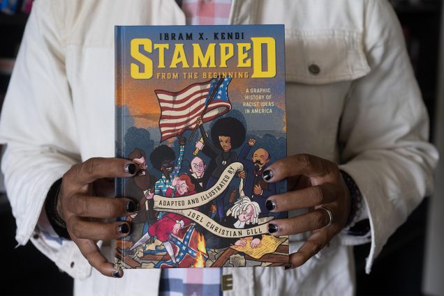 Photo: Two hands with black painted fingernails hold a copy of "Stamped from the beginning", a graphic novel adapted from Dr Ibram X Kendi’s book