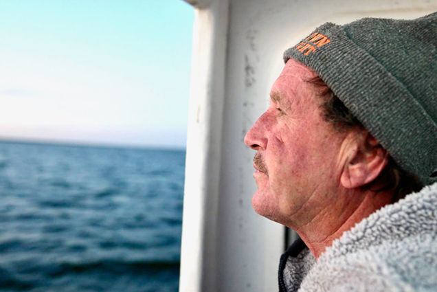 Photo: A man with a moustache wearing a beanie looks out over the open ocean on a boat