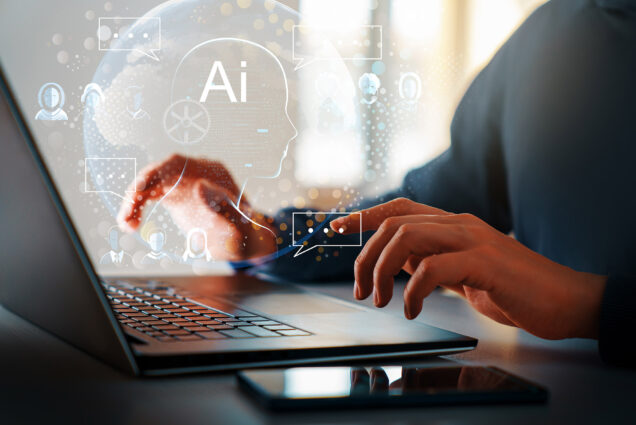 Photo: The concept of artificial intelligence and computer technology is shown with a photo of a person typing on a black laptop. AI techno-themed illustrations hover above the hands as they type, signifying the use of AI.