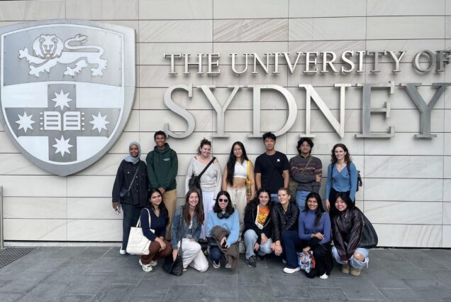 Photo: A group of college students in casual attire stand in front of a sign that reads "University of Sydney"