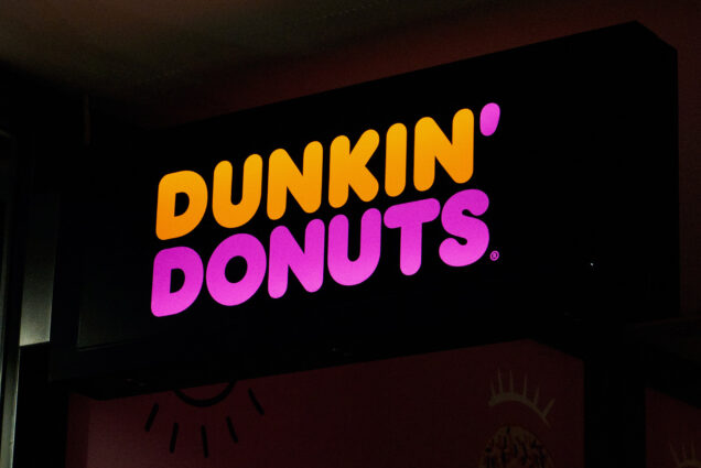 Photo: Illuminated Dunkin' Donuts Sign is shown during a dark night. Photo is zoomed in to show the iconic sign.