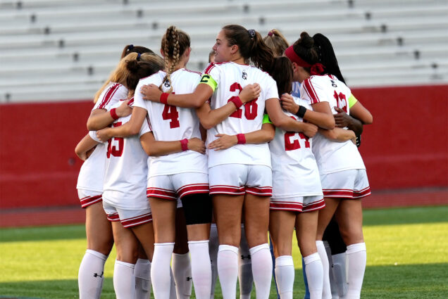 Photo: The BU Women's soccer team in red and white jerseys huddle at a recent match