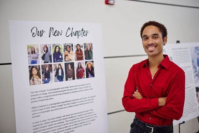 Photo: Will Chapman, a young person with short dark hair and a moustache and large smile on their face stands next to a posterboard reading "Our New Chapter" at a recent photography showcase