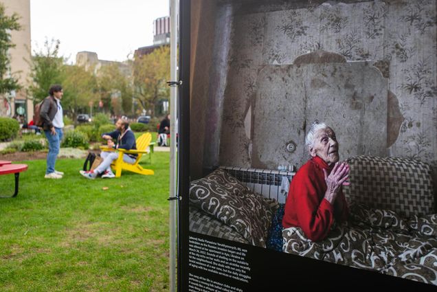 Photo: Closeup photo of an older Ukrainian woman in bed during wartime. The photo is juxtaposed against the scene of students hanging out on BU's COM Lawn.