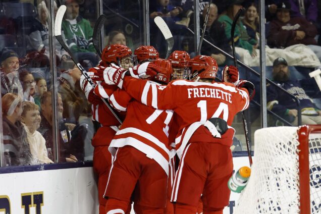 Photo: A group of four men dressed in red BU hockey gear hug and embrace on the ice rink at the end of a game.