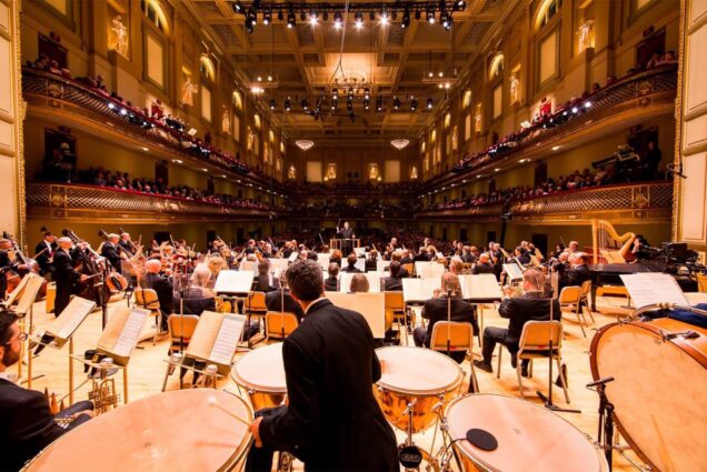 Photo: Perspective from behind an orchestra on stage at the Boston Symphony, looking out over the audience and into an ornate theatre