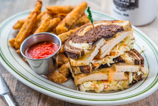 Photo: a Decadent corned beef sandwich on a plate with fries in a well light bright restaurant