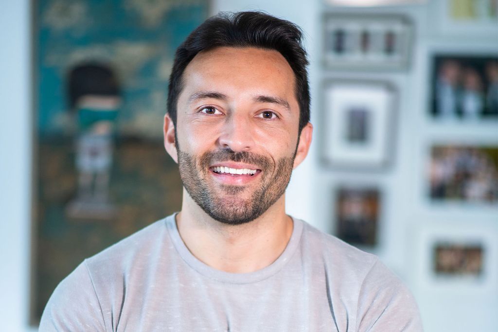 Photo: A man with short dark hair and a beard smiles for a closeup portrait