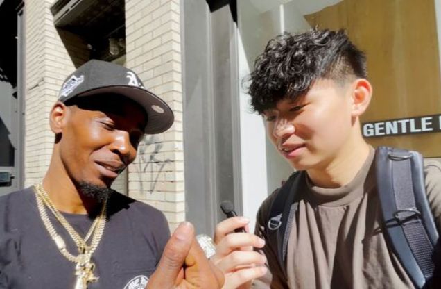 Close-up photo of Boston University student Gavin Cheng (Questrom'25) and a random person on the street. He is holding a mini microphone and wearing a brown shirt. The man to the left is wearing multiple chains, a black hat, and a black t-shirt.