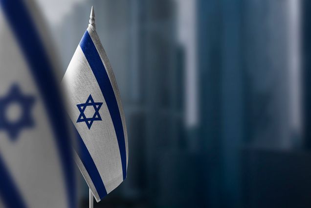 Photo: Small flags of Israel are displayed in front of a blurry background of a city.