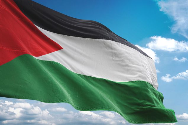 Photo: A Palestinian flag is shown waving across a blue sky. A few stray clouds can be seen in the sky.