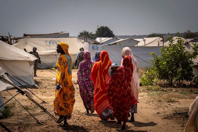 Photo: A group of woman walk in a refugee camp, one with her child wrapped in bright, beautiful garments.