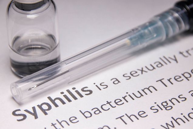 Photo: A stock photo of a needle, a bottle of liquid, and text that reads Syphilis.