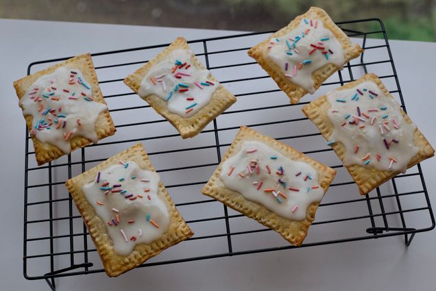 Photo: A overhead shot of six homemade hand pies, similar to Pop Tarts, cool on a wire tray. Beneath them, a white, clean surface.