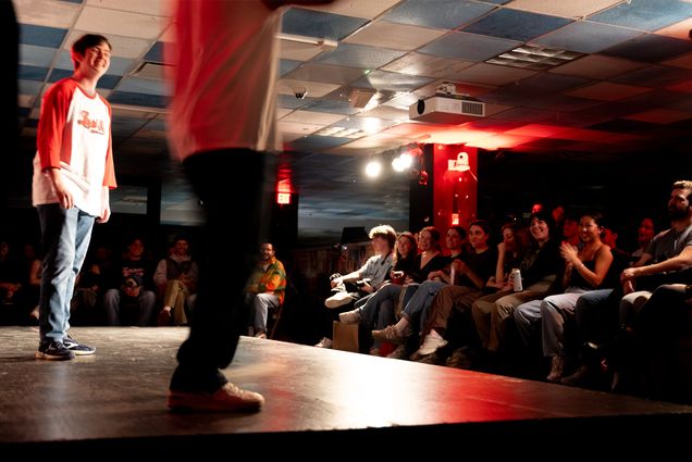 Photo: Two performers on stage wearing white shirts with red long sleeves. They are in front of a crowd of people