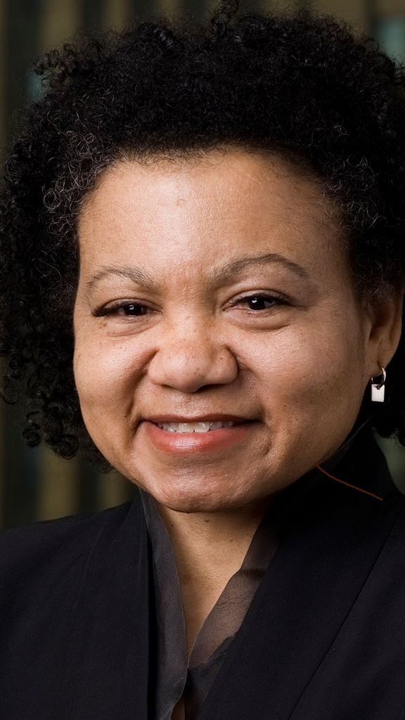 Photo: Headshot of a woman with dark hair wearing a black suit jacket and smiling