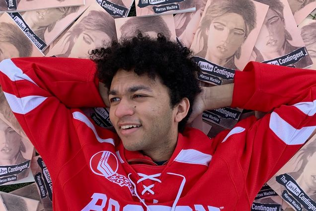 Photo: Marcus Wachira, a young man, with his hands behind his head and BU jersey laying on top of his artwork.