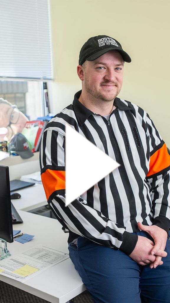 Photo: A man in a referee outfit with a hat and a long-sleeved shirt with vertical black and white stripes. There is a white play button in the center of the image