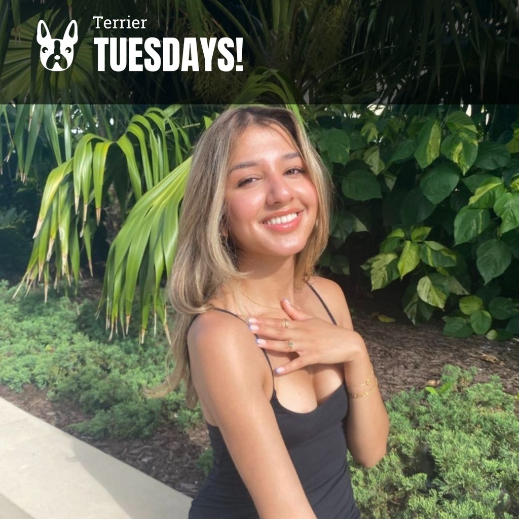 Photo: A young woman with bleached blonde hair smiles in a black top in a tropical area.