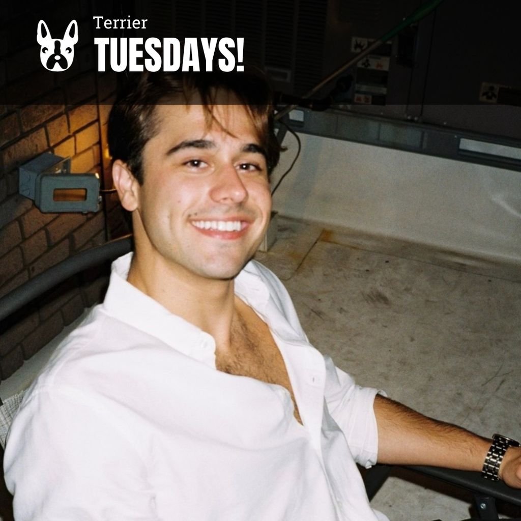 Photo: A young man smiles for a photo wearing a white button up thats lowly unbuttoned.