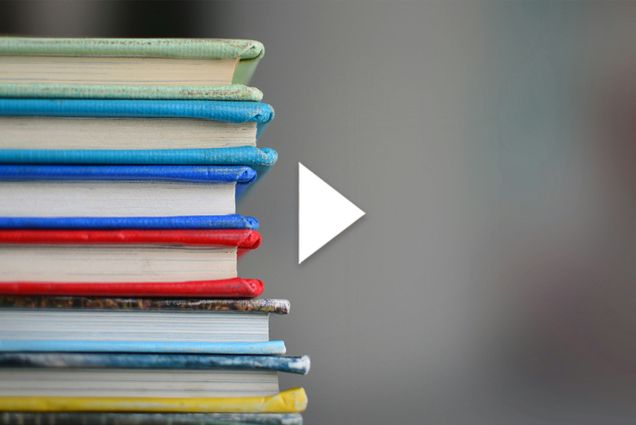 Photo: A stack of hardcover books of various colors. There is a white play button overlayed on top of the image