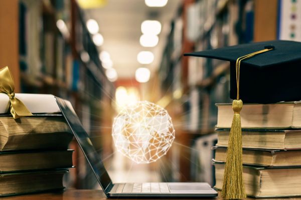 Photo: A picture of an open laptop with a glowing orb hovering above it. To its left there is a diploma wrapped in gold ribbon and to its right there is a graduation cap. Both are on top of stacks of books