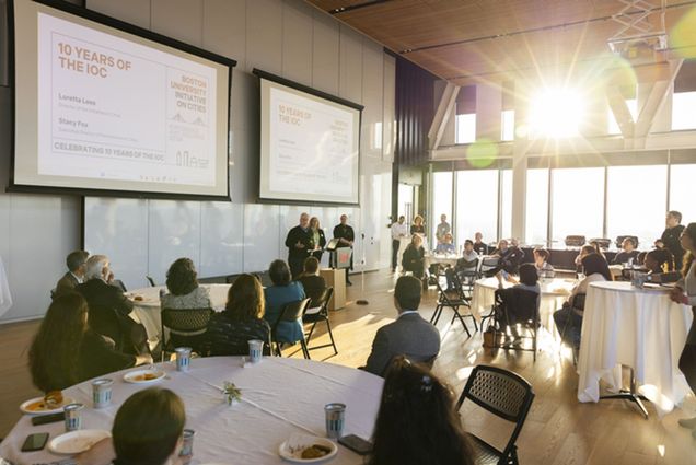 Photo: A group of people watching a presentation and sitting at circular tables with white table cloths