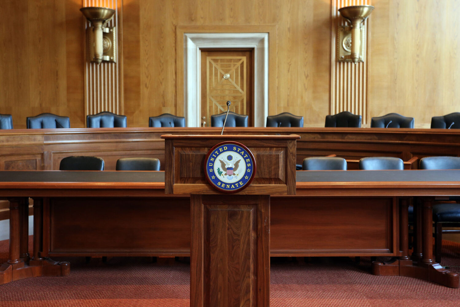 Photo: A picture of a podium with the words "United States Senate" on it. Behind the podium there are tables and chairs