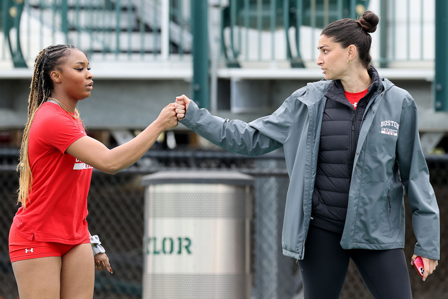 Photo: Two woman fist bumping each other at a track meet. Reigning Patriot League Indoor Women’s Field Athlete of the Meet Peace Omonzane (CAS’26) fistbumps jumps and multis coach Sara Macey.