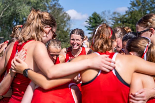 Photo: The BU women's cross country team huddling and smiling while wearing red uniforms