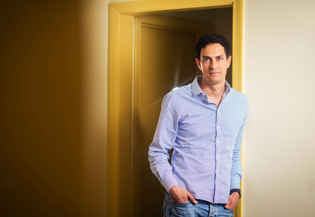 Photo: A picture of a man posing in front of an open door. He is wearing a button down shirt