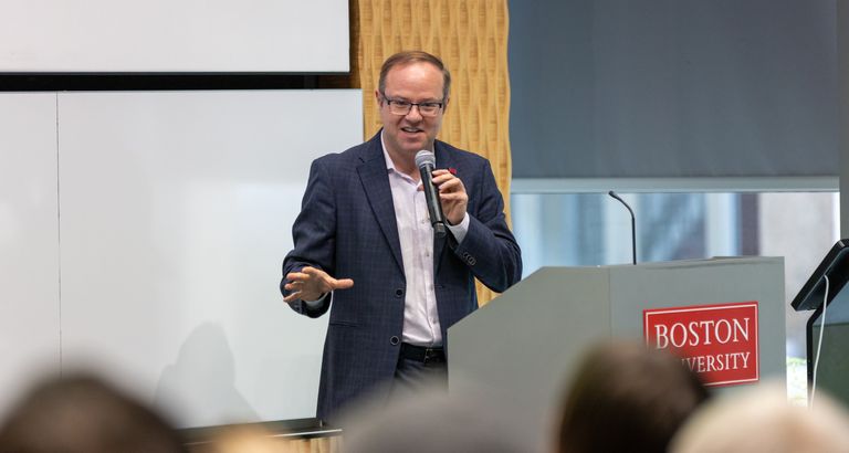 Benjamin Sovacool holds a mic at a BU podium.