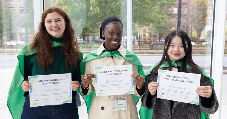 Three BU students posing in green capes holding award certificates.