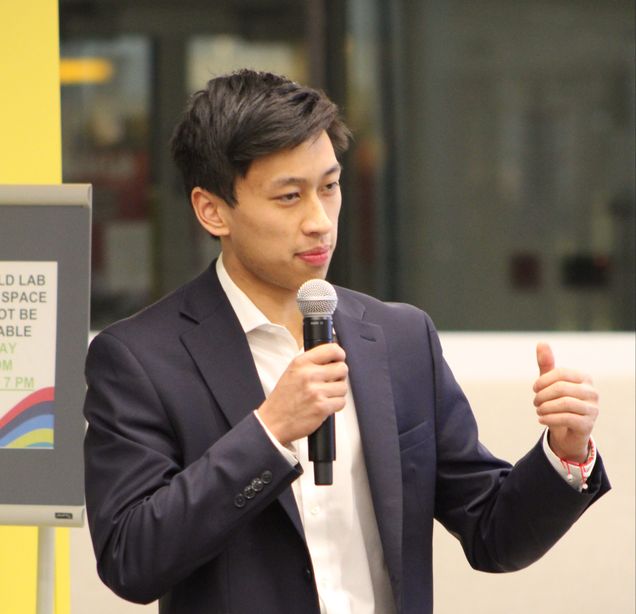 Kevin Tang holding a microphone while presenting a pitch to an audience.