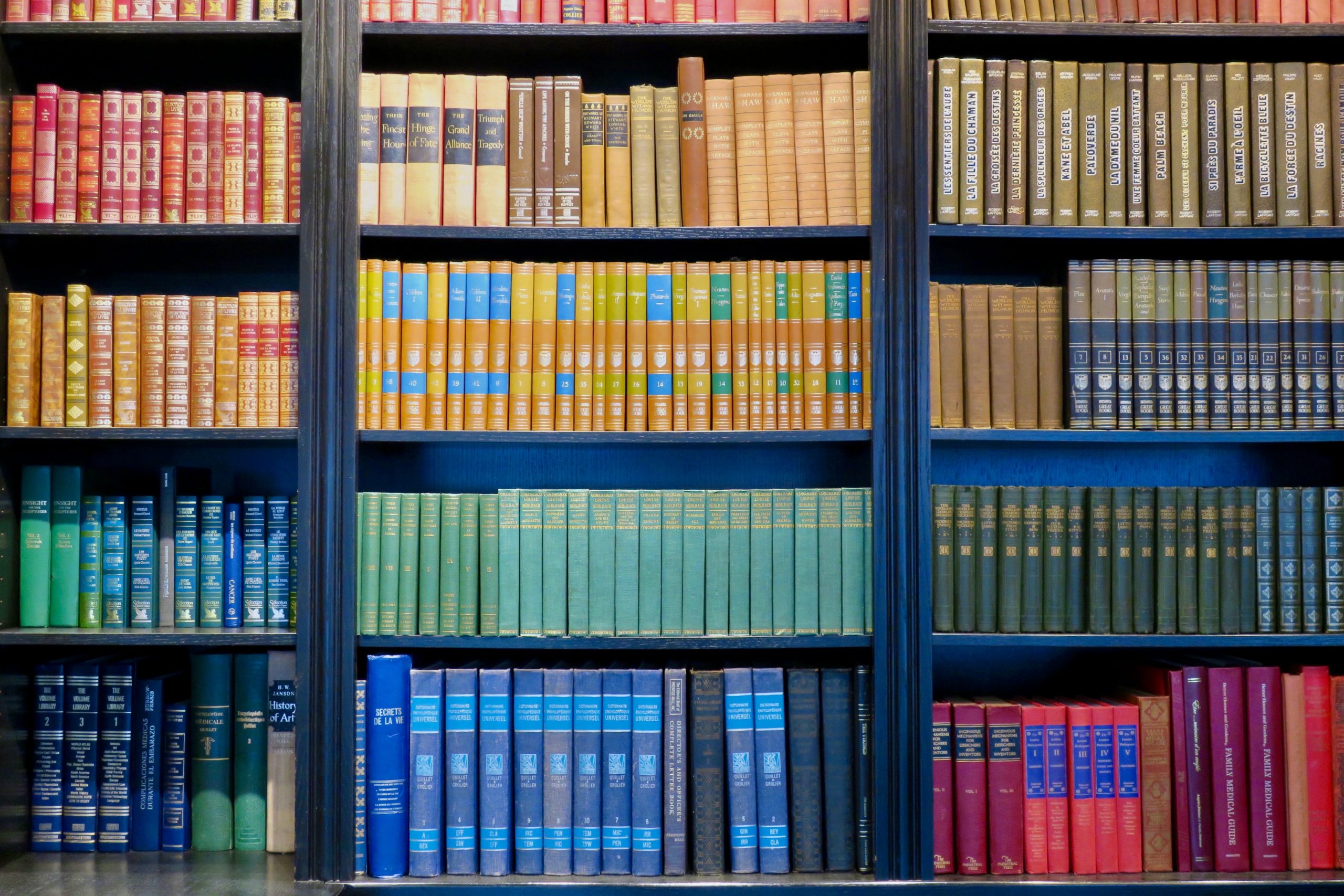 color coordinated satisfying bookshelf, shades of red yellow, green, blue and brown