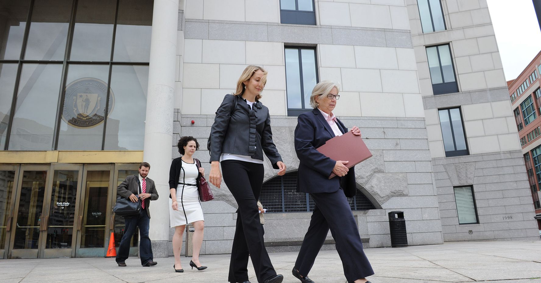 Four people in business attire walk outside of a courthouse in Massachusetts.