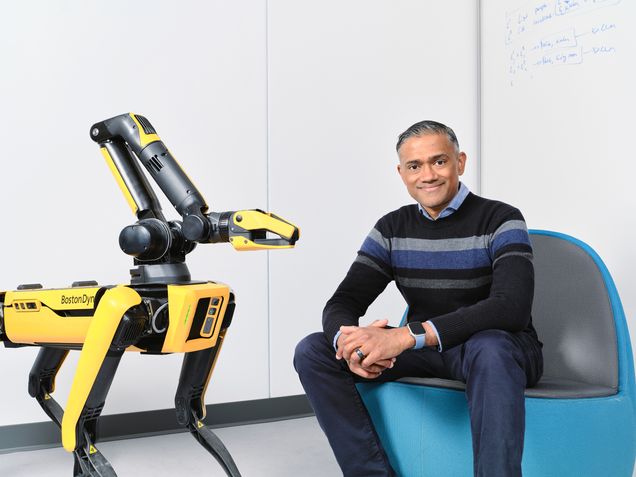 Vasanth Sarathy ('10) sits in a blue chair with a robot next to him