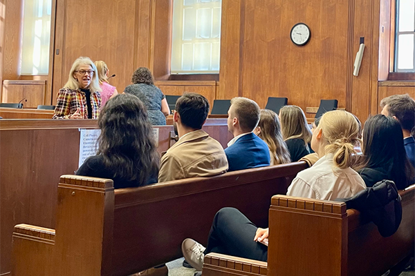 A dozen law students sit in a courtroom listening to a professor speak.