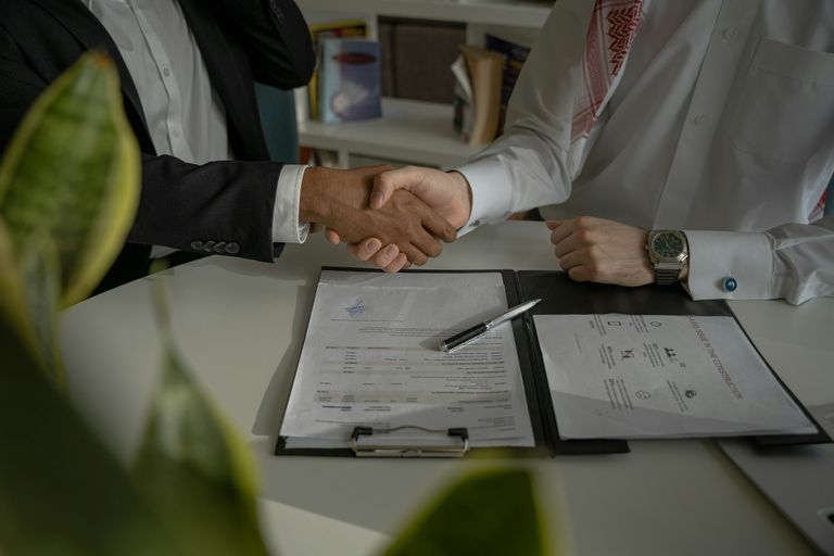 The forearms and clasped hands of two men making a deal over paperwork