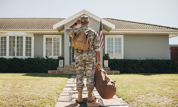 Rearview of a soldier returning home from the army. He is standing in front of his home with his luggage