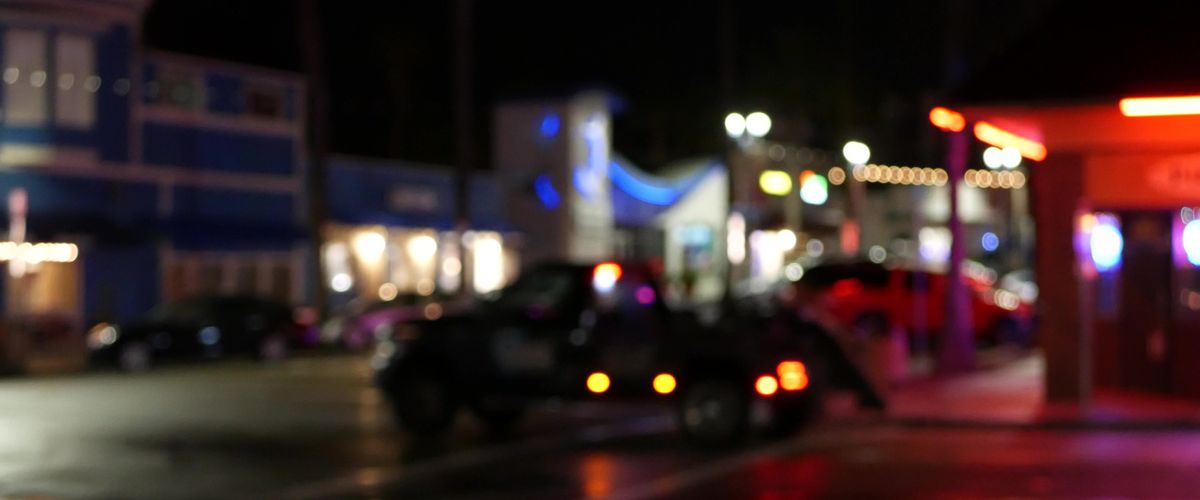 Defocused evening street, blurred bokeh. Lights of city and cars on rainy night. Reflection of electric lamps. Automobiles on road in soft focus. Twilight illuminated town, Oceanside, California USA.