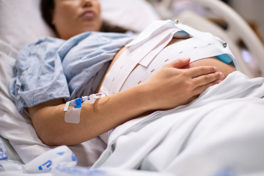 A pregnant woman in the hospital with an IV drip and a cardiograph.