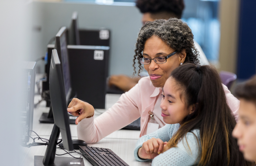 Shows a teacher and a student at a computer