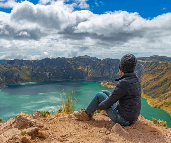 student sitting on a mountain ridge looking inot a lake in the crater