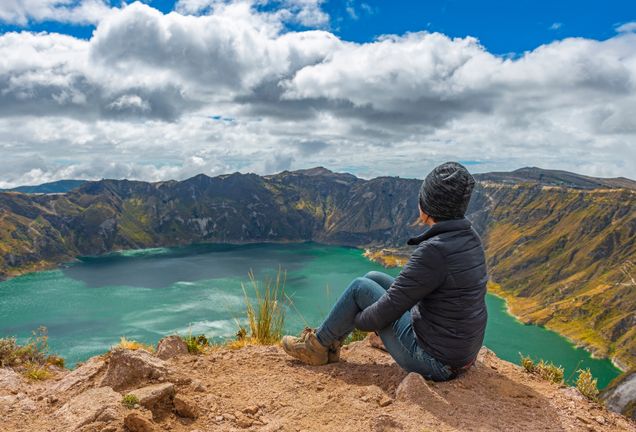 student sitting on a mountain ridge looking inot a lake in the crater