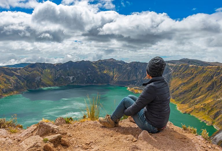 student sitting on a mountain ridge looking inot a lake in the crater