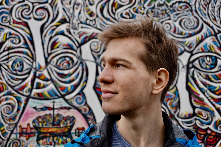 male student in profile in front of of a mural on the berlin wall